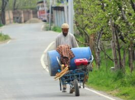 With crops sprayer on his pushcart, a farmer heads towards his orchards.