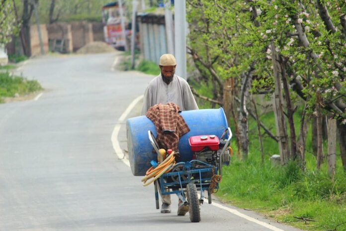 With crops sprayer on his pushcart, a farmer heads towards his orchards.