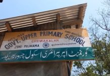 Pulwama’s young students endure scorching heat as school construction stalls School Signboard Clinging to a Tin Shed