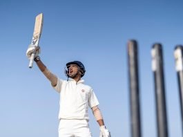 A young cricketer waving his bat to the spectators after achieving a feat