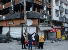 People gathered at a corner in Tehran, near a building showing substantial damage.