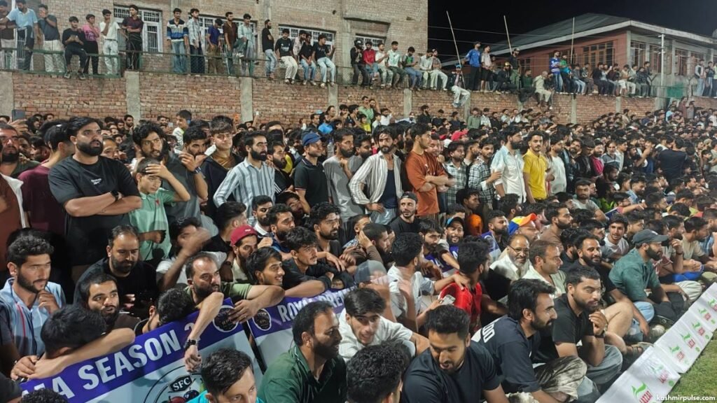 Enthusiastic spectators climb a section of a stadium wall to watch the game in Sports Stadium Pulwama
